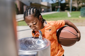 a boy holds a basketball while drinking from a bubbler